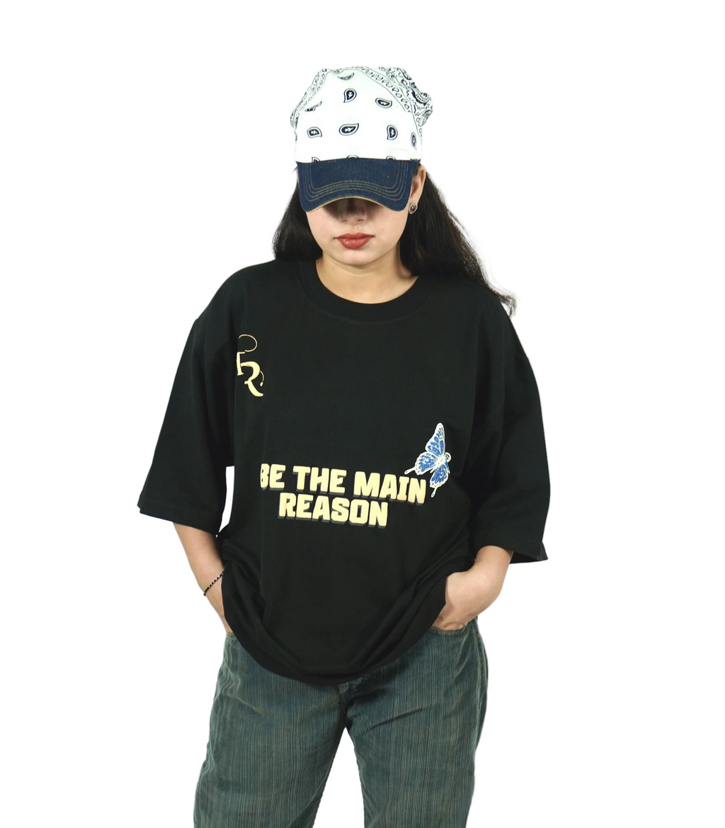 TAMRAT Black Boxy Fit T-shirt with 'Be The Main Reason' graphic and blue butterfly print worn with a cap